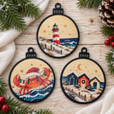 Drei maritime Weihnachtsanhänger mit schwarzem Rahmen: Leuchtturm, Weihnachtskrabbe und Strandhäuschen auf hellem Holz