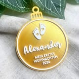 Eine goldene 3D-gedruckte Christbaumkugel mit weißer Aufschrift Alexander, Babyfüßen und dem Text Mein erstes Weihnachten 2026.