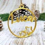 Ein goldener, 3D-gedruckter Weihnachtsanhänger mit dem Namen Luca und zwei Sternen auf hellem Holz mit Tannenzapfen.