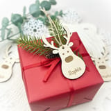 Personalisierter Holzrentier-Anhänger auf einem roten Geschenk.