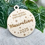 Holzanhänger Mein erstes Weihnachten mit dem Namen Maximilian und der Jahreszahl 2025 vor Efeublättern