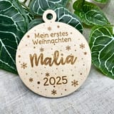 Holzanhänger Mein erstes Weihnachten mit dem Namen Malia und der Jahreszahl 2025 vor Efeublättern