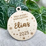 Holzanhänger Mein erstes Weihnachten mit dem Namen Elias und der Jahreszahl 2025 vor Efeublättern