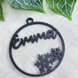 Schwarze Weihnachtskugel mit dem Namen Emma und Schneeflockenmotiv vor Efeu