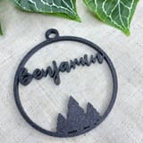 Schwarze Weihnachtskugel mit dem Namen Benjamin und Tannenmotiv vor Efeu