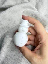 Weißer Schneemann in einer Hand vor hellem Stoff