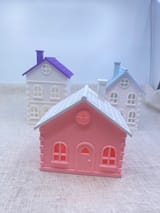 Drei gedruckte Winterhäuser: rosa Landhaus, weißes Stadthaus mit violettem Dach und weißes Giebelhaus mit blauem Dach