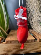Ein leuchtend rotes, 3D-gedrucktes Schlittschuh-Ornament mit einem glatten, abgerundeten Stiefeldesign und einer kleinen Kufe an der Unterseite. Der Schlittschuh ist mit einem weißen Band geschnürt, das vorne zu einer Schleife gebunden ist.