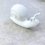 Originalfoto von Ninas weiß gedruckter Leuchtschnecke in Seitenansicht mit aufgesetztem geripptem Spiralhaus auf hellem Stoff.