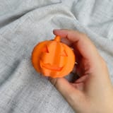 Orangefarbener Halloween-Kürbis mit Gesicht in einer Hand