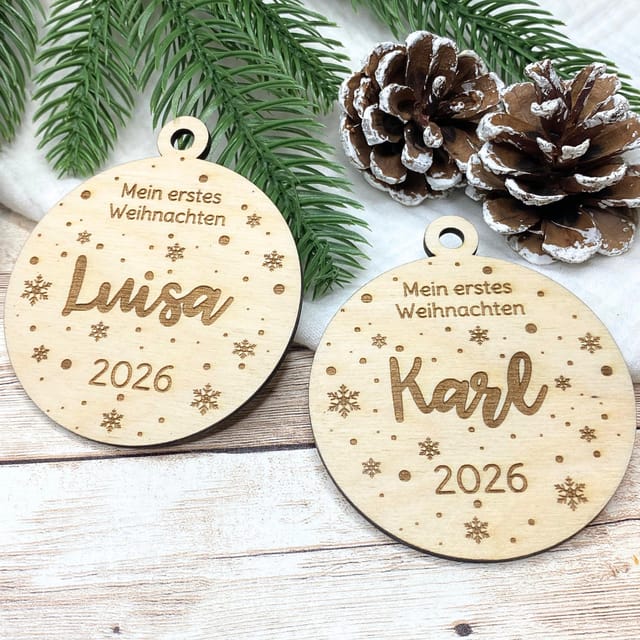 Zwei Holzanhänger Mein erstes Weihnachten mit den Namen Luisa und Karl und der Jahreszahl 2026 neben Tannengrün und Zapfen
