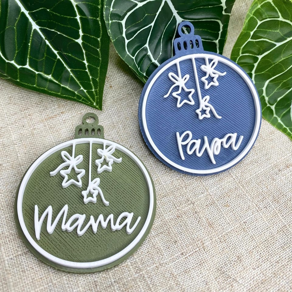 Personalisierte PLA-Kugeln Mama und Papa in Grün und Blau auf hellem Stoff.