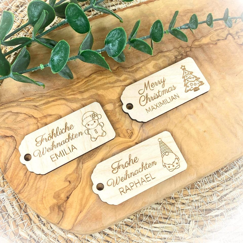 Personalisierte Holz-Geschenkanhänger mit weihnachtlichen Schriftzügen auf Holzuntergrund.