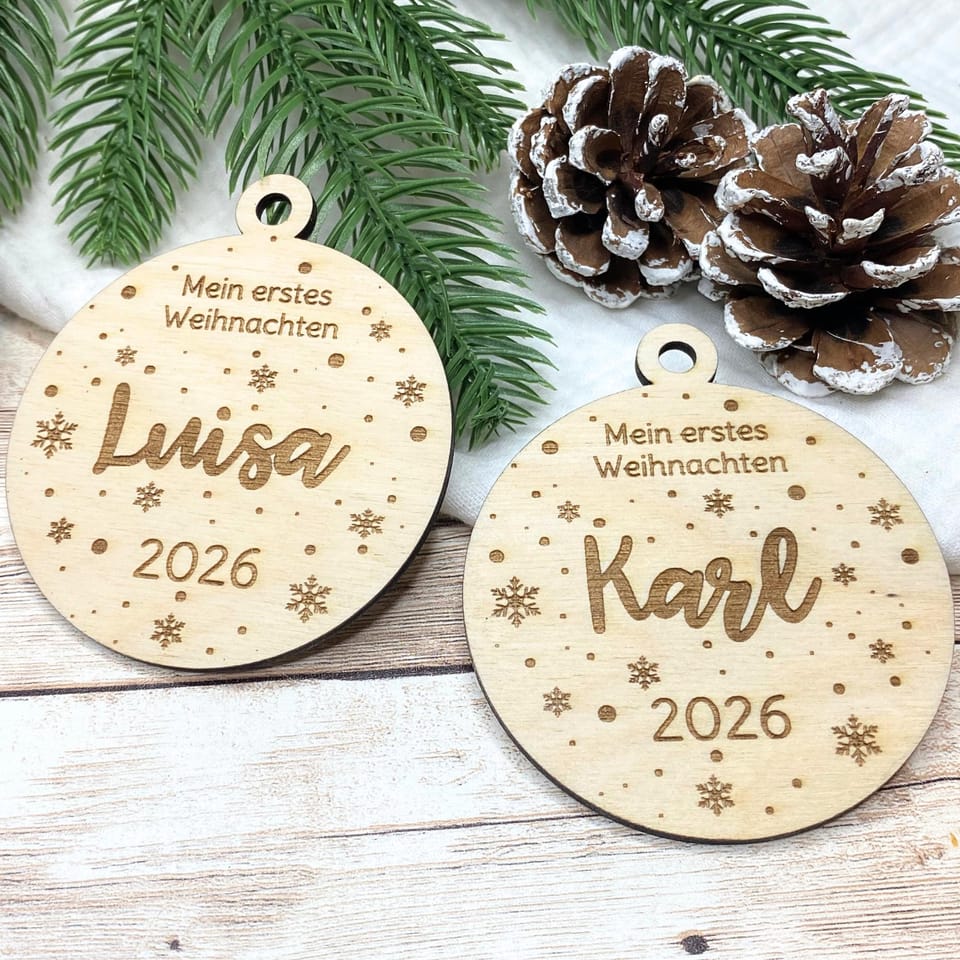 Zwei Holzanhänger Mein erstes Weihnachten mit den Namen Luisa und Karl und der Jahreszahl 2026 neben Tannengrün und Zapfen